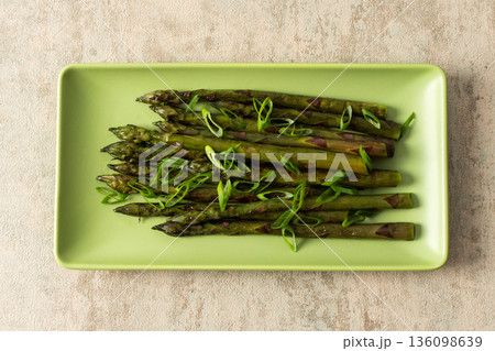 Asparagus spears are arranged neatly on a green plate, garnished with sliced green onions. This dish represents a simple yet flavorful vegetable choice for any meal Asparagus spears are arranged neatly on a green plate, garnished with sliced green onions. This dish represents a simple yet flavorful vegetable choice for any meal 136098639