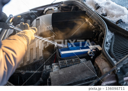 Man replacing car battery in winter cold with open hood during roadside emergency repair, emergency vehicle maintenance concept Man replacing car battery in winter cold with open hood during roadside emergency repair, emergency vehicle maintenance concept 136098711