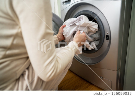 Daily chores. Smart appliances. Woman lading or unload white clothes from washing machine at home Daily chores. Smart appliances. Woman lading or unload white clothes from washing machine at home 136099033
