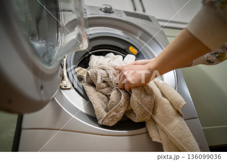 Washing machine at home. Smart appliances. Woman loading the washing machine with towels. Daily chores. Cleaning laundry Washing machine at home. Smart appliances. Woman loading the washing machine with towels. Daily chores. Cleaning laundry 136099036
