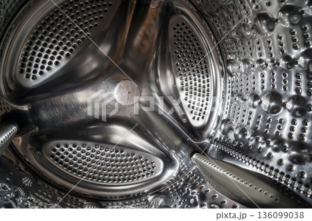 Stainless steel washing machine drum interior with perforated metal texture. Household appliance detail showing modern technology. Smart home appliances. Stainless steel washing machine drum interior with perforated metal texture. Household appliance detail showing modern technology. Smart home appliances. 136099038