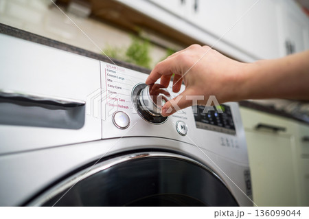 Smart home appliances. Adjusting washing machine setting. Hand turning the dial of a modern washing machine. Daily chores 136099044