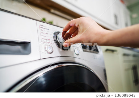 Smart home appliances. Adjusting washing machine setting. Hand turning the dial of a modern washing machine. Daily chores Smart home appliances. Adjusting washing machine setting. Hand turning the dial of a modern washing machine. Daily chores 136099045