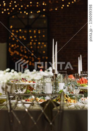 Elegant banquet table with candles and food in festive hall with warm bokeh lights Elegant banquet table with candles and food in festive hall with warm bokeh lights 136099398