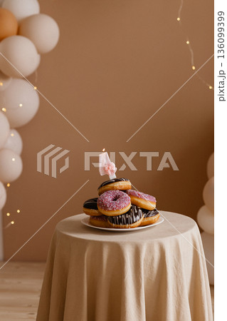 Donut cake with number four candle on table against beige wall with balloons and lights Donut cake with number four candle on table against beige wall with balloons and lights 136099399