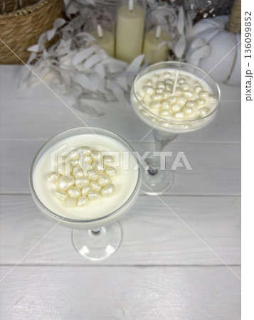 White candles in a glass candle holder. Wax pearls near the wick. The candles are standing on white boards. Oblique Angle. White candles in a glass candle holder. Wax pearls near the wick. The candles are standing on white boards. Oblique Angle. 136099852