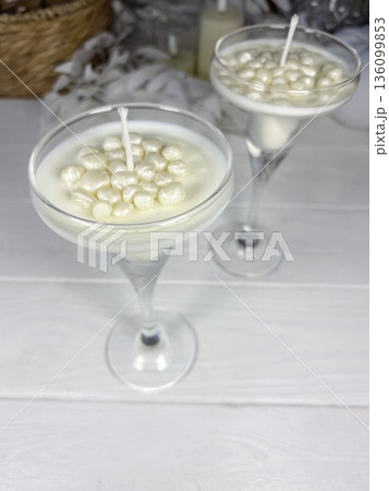 White candles in a glass candle holder. Wax pearls near the wick. The candles are standing on white boards. 136099853