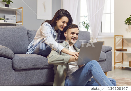 Laughing happy couple watching funny video or using laptop for social media at home. Laughing happy couple watching funny video or using laptop for social media at home. 136100167
