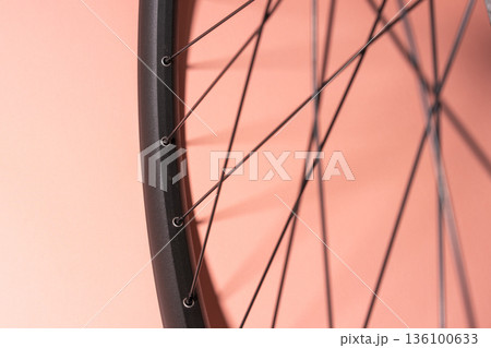 Black bicycle rim with thin metal spokes casting shadows on a pink background. 136100633