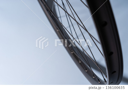 Close-up of a black bicycle rim with spokes against a smooth light blue background. Close-up of a black bicycle rim with spokes against a smooth light blue background. 136100635