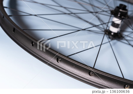Close-up of a black bicycle wheel rim with spoke holes and tensioned spokes on a blue background 136100636