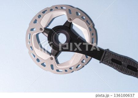 Close-up of a metallic bicycle disc brake rotor attached to a black handle on a blue background Close-up of a metallic bicycle disc brake rotor attached to a black handle on a blue background 136100637