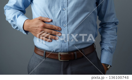 男性がオフィス風の服装でお腹に手を当てる日中の室内描写 136100748