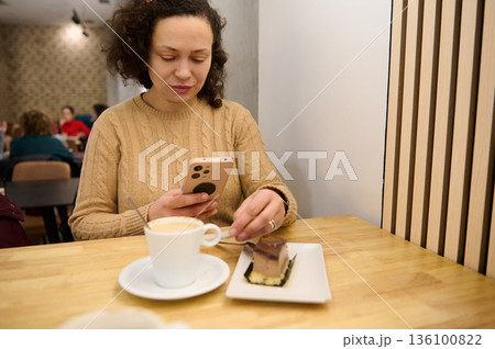 Woman In Beige Knit Sweater Using Smartphone At Cafe Table With Coffee And Dessert Woman In Beige Knit Sweater Using Smartphone At Cafe Table With Coffee And Dessert 136100822