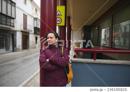 Woman in Burgundy Winter Coat Standing on City Street Near Red Pillar and Signage Outdoor 136100829