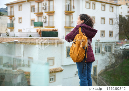 Woman With Orange Backpack On Balcony Overlooking City Buildings In Rain Woman With Orange Backpack On Balcony Overlooking City Buildings In Rain 136100842