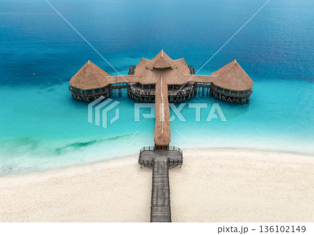 Aerial top down view of sea and wooden pier with thatched roof 136102149