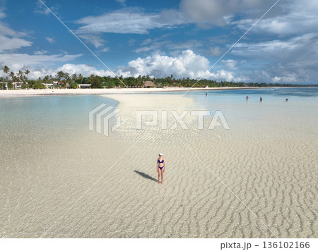 Woman in bikini stands on a white sandbank during low tide 136102166