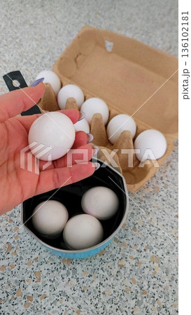 The woman carefully holds an egg in her palm, a ladle of water is ready for boiling eggs. The woman carefully holds an egg in her palm, a ladle of water is ready for boiling eggs. 136102181