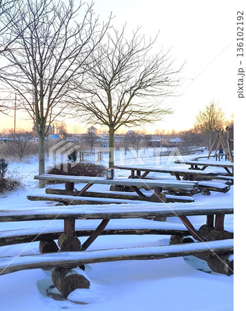Wooden tables and benches in a winter park against the backdrop of the sunset sky Wooden tables and benches in a winter park against the backdrop of the sunset sky 136102192