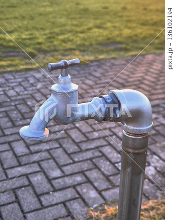 A street metal water tap against the backdrop of paving stones in a park 136102194