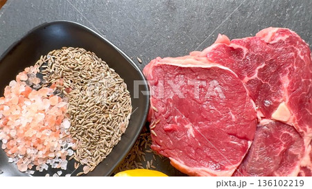 Closeup Spices And Raw Steak With Lemon Half And SaltPepper Mixture In Pan, Tactile Textures, Moody Contrast, IngredientFocused Still Life For Culinary Projects Closeup Spices And Raw Steak With Lemon Half And SaltPepper Mixture In Pan, Tactile Textures, Moody Contrast, IngredientFocused Still Life For Culinary Projects 136102219