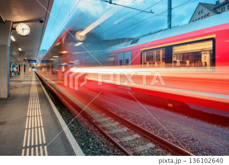 Blurred red passenger train passing mountain railway station Blurred red passenger train passing mountain railway station 136102640