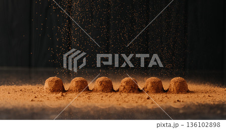 Cocoa powder falling over chocolate truffles with reflection on black background 136102898
