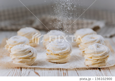 Powdered sugar falling on vanilla zephyr rosettes on parchment, rustic background 136102900