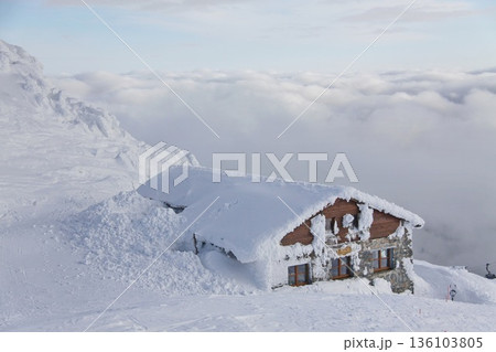 Snow-covered alpine mountain hut nestled on a high ridge. Snow-covered alpine mountain hut nestled on a high ridge. 136103805