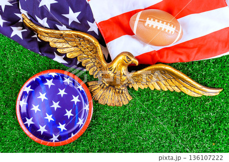Eagle decoration rests on grass an American flag super bowl suggesting festive gathering event. Eagle decoration rests on grass an American flag super bowl suggesting festive gathering event. 136107222