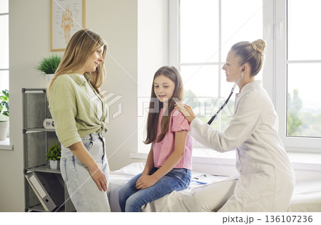 Mother and pediatrician with stethoscope during child checkup in clinic room 136107236