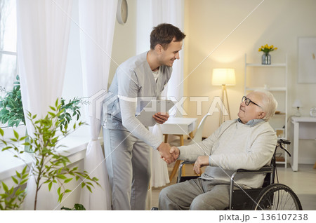 Doctor Shaking Hands With Elderly Patient In Wheelchair During Consultation 136107238