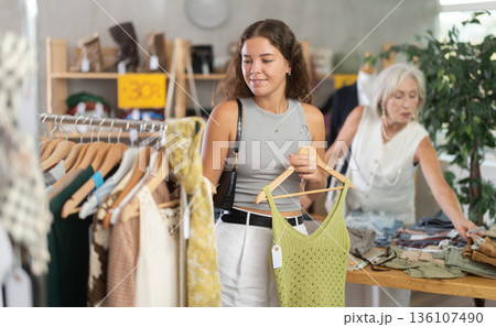 Positive young woman choosing something for summer in clothing store 136107490