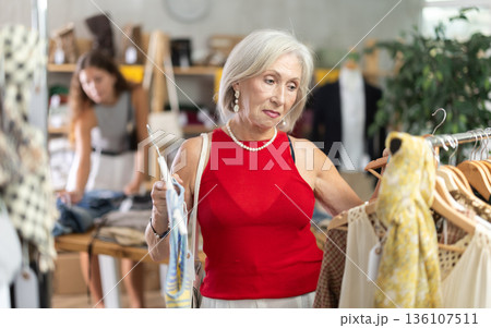 Elderly woman choosing vest in clothing store Elderly woman choosing vest in clothing store 136107511