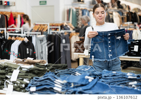 Young girl choosing jean skirt in clothing store 136107612