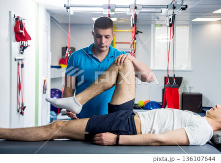 Rehabilitation therapy. Physiotherapist working with young male patient Rehabilitation therapy. Physiotherapist working with young male patient 136107644