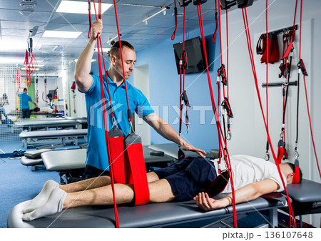 Physiotherapy. Suspension training therapy. Young man doing fitness traction Physiotherapy. Suspension training therapy. Young man doing fitness traction 136107648