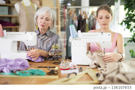 Two female dressmakers working with sewing-machine in tailor's workshop 136107655