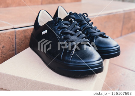 Elegant black leather womens shoes blank product for branding displayed on recycled cardboard box. New casual female sneakers no-brand footwear e-commerce. No logo product 136107698