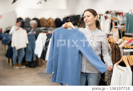 Middle-aged woman choosing convenient jumper in clothing store Middle-aged woman choosing convenient jumper in clothing store 136107718