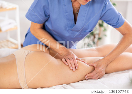 Masseuse doing thigh massage to young woman 136107748