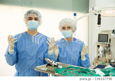 In operating room of veterinary clinic, two experienced doctors are standing in surgical suits In operating room of veterinary clinic, two experienced doctors are standing in surgical suits 136107796