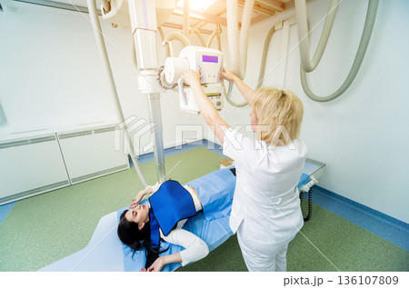 Radiologist and patient in a x-ray room. Classic ceiling-mounted x-ray system. Radiologist and patient in a x-ray room. Classic ceiling-mounted x-ray system. 136107809