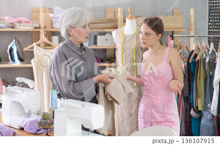 Mature woman scolding young tailoress in sewing studio Mature woman scolding young tailoress in sewing studio 136107915
