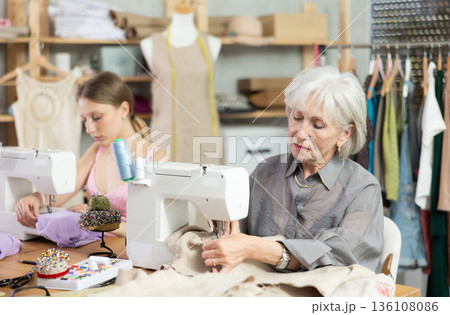 Two seamstresses sitting and working in the workshop Two seamstresses sitting and working in the workshop 136108086
