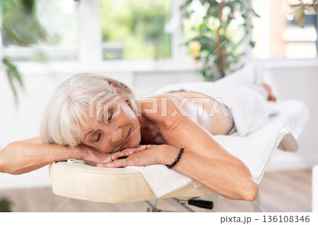 Mature female client of massage parlor lies with legs covered with towel Mature female client of massage parlor lies with legs covered with towel 136108346