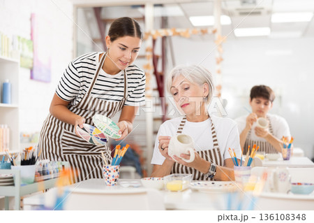 Young girl assisting senior woman painting ceramic mug in pottery class Young girl assisting senior woman painting ceramic mug in pottery class 136108348