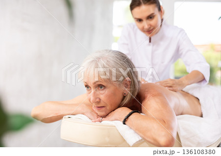 Blurry unrecognizable woman performs shoulder massage to female client. 136108380