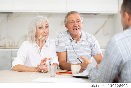 Salesman seller shows on laptop details of purchase to elderly couple. 136108403